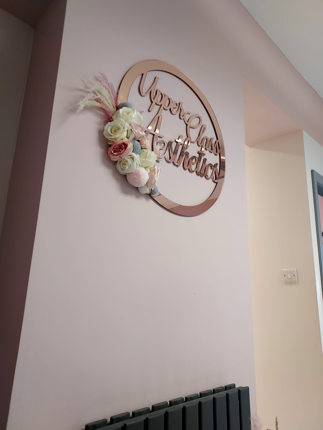 The rose gold Upper Class Aesthetics sign on the clinic wall