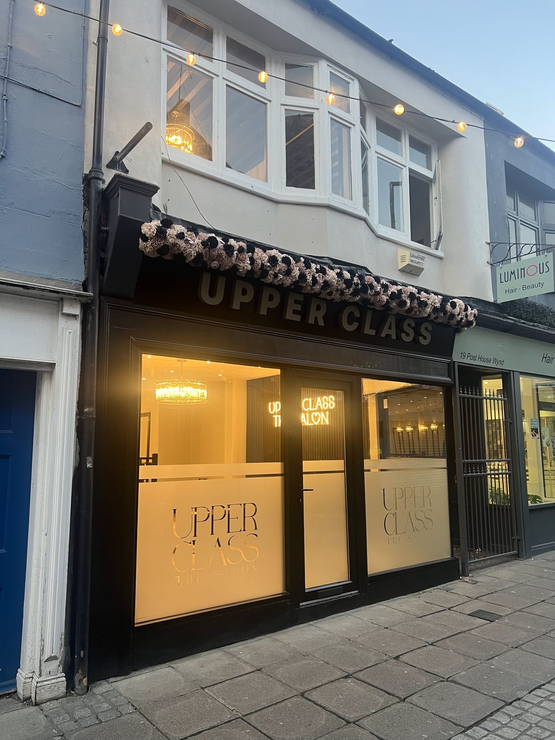 The Upper Class shopfront on Post House Wynd at dusk