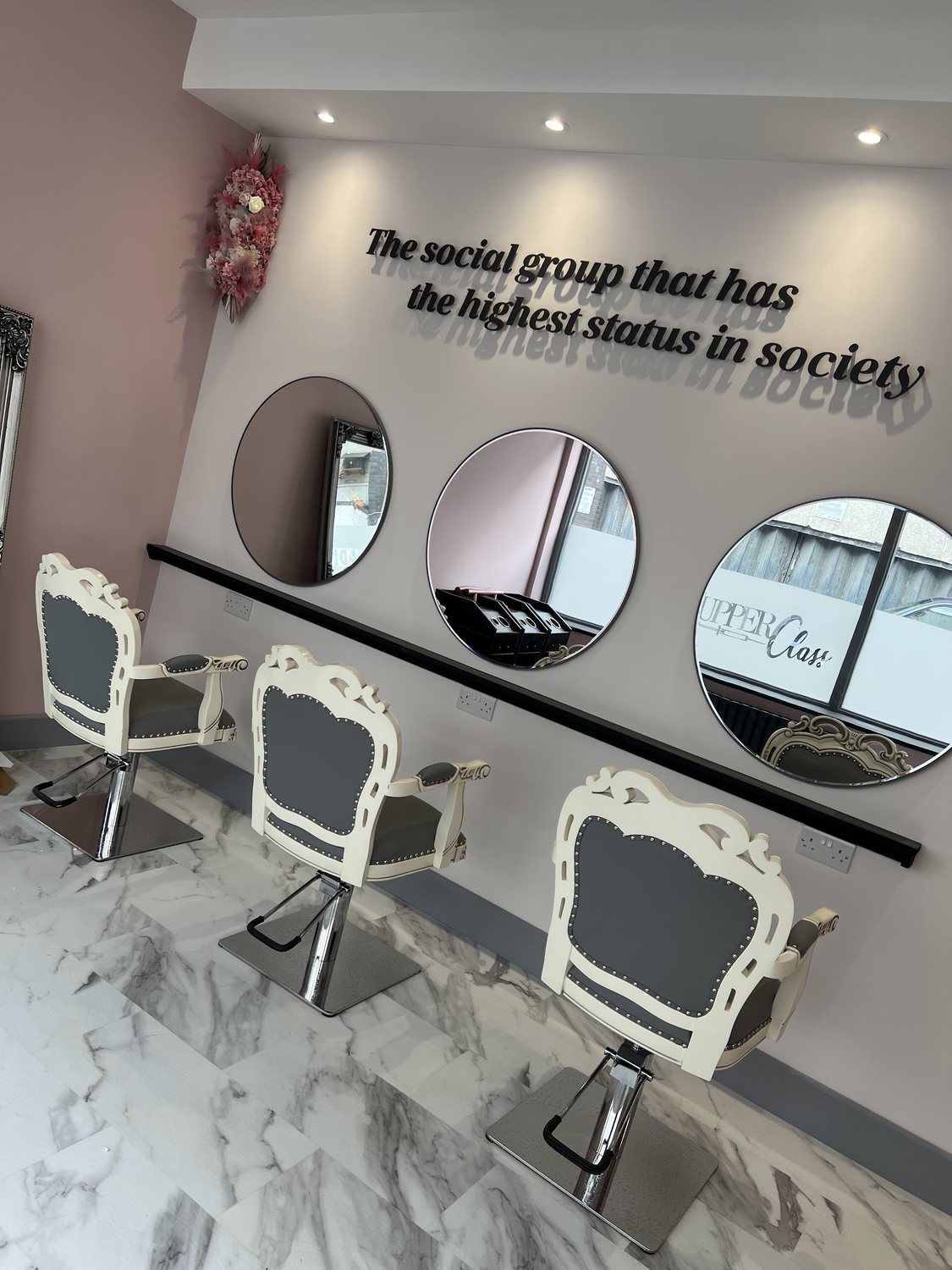 Three salon chairs beneath wall lettering that reads: the social group that has the highest status in society